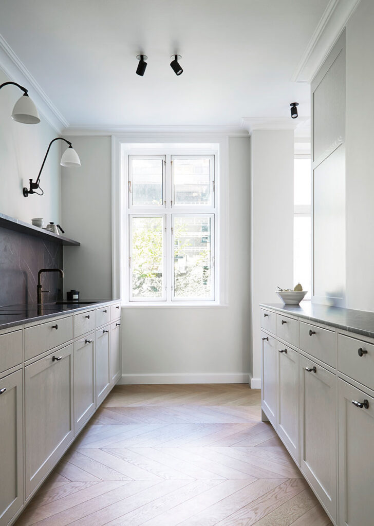 Long kitchen area with cabinets and drawers, looking towards a large window.